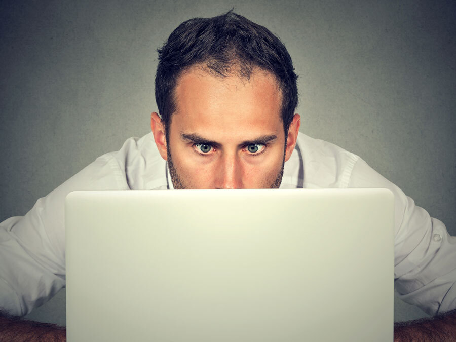 Ein Mann schaut schockiert auf den Bildschirm seines Laptops. Er hat soeben eine erhöhte Drittanbieterrechnung erhalten.
