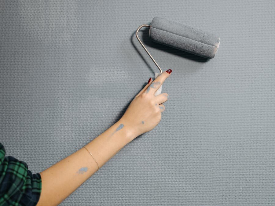 Eine Hand hält eine Malerrolle mit grauer Farbe. Es werden Schönheitsreparaturen ausgeführt.