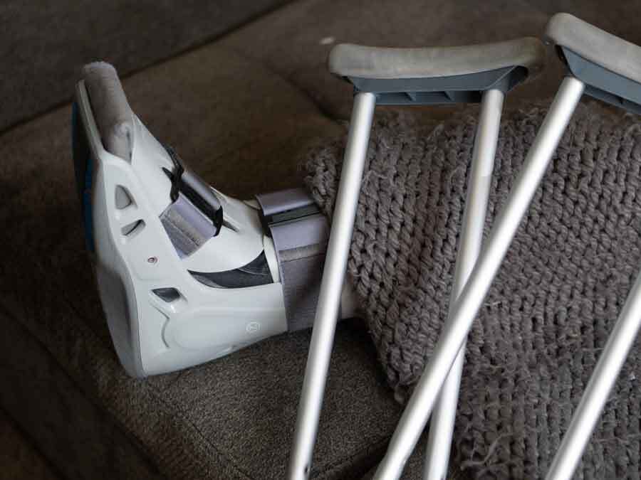 Ein Fuß mit Bandagen und zwei Krücken auf einem Sofa. Hier hatte jemand einen Arbeitsunfall im Homeoffice.