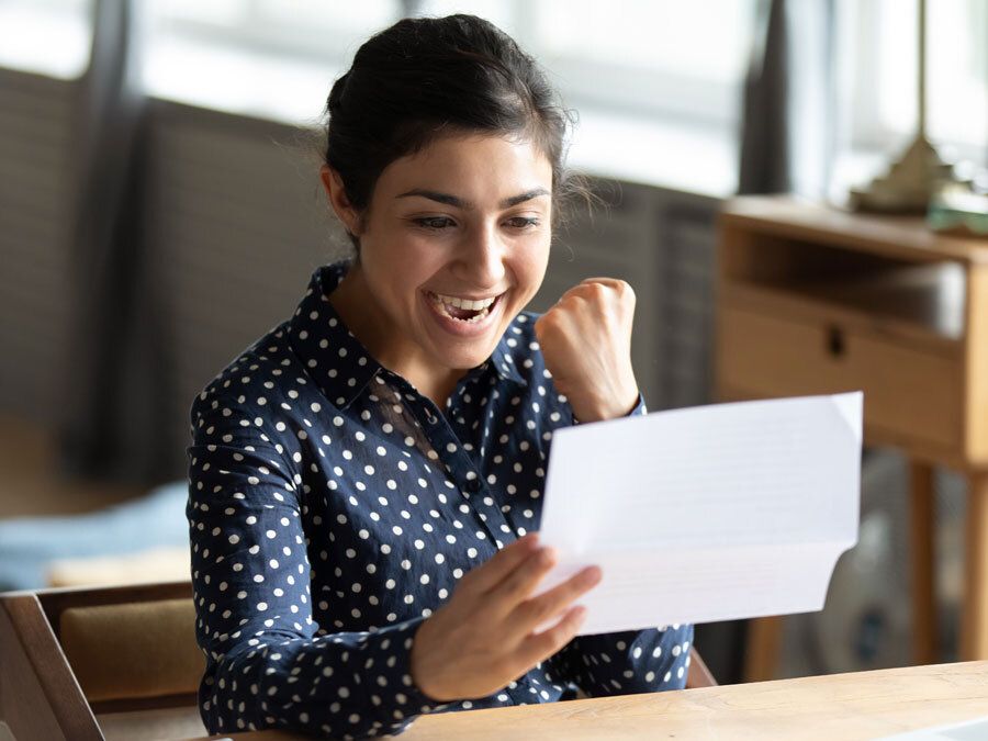 Eine Frau hält einen Brief in der Hand und freut sich. Ihre Bitte um eine Gehaltserhöhung hat Gehör gefunden.