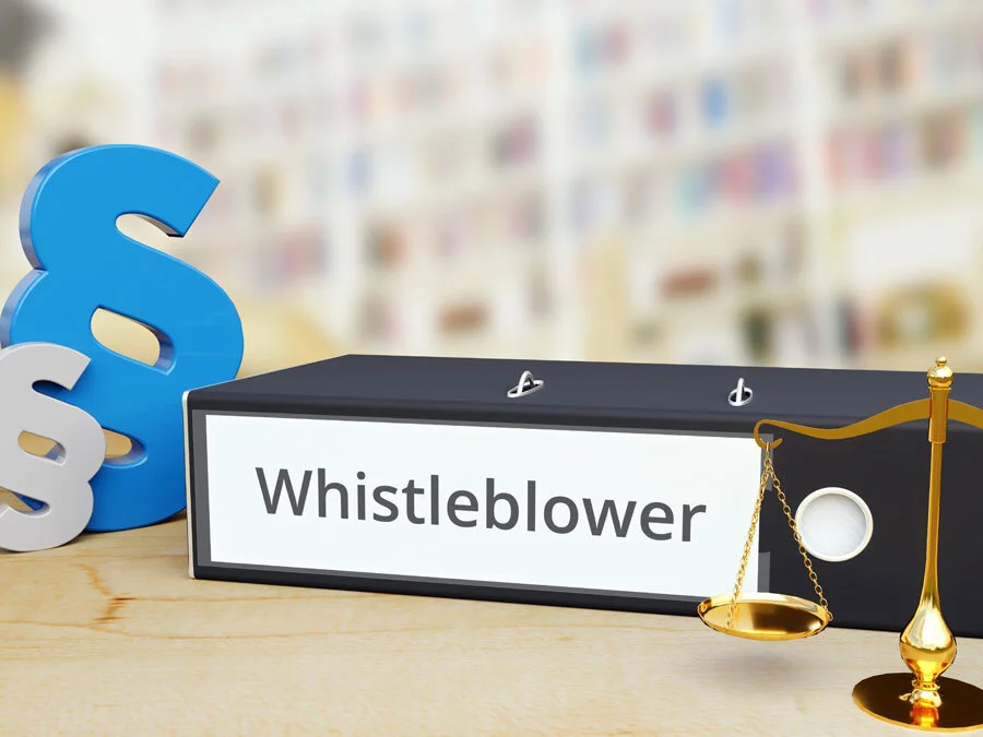 Paragraphenzeichen und eine Waage stehen symbolisch neben einem Ordner mit der Aufschrift Whistleblower.