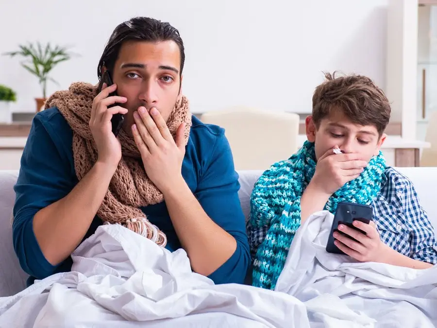 Vater und Sohn liegen mit einem Smarphone in der Hand krank im Bett. Für beide ist die telefonische Krankschreibung nun möglich.